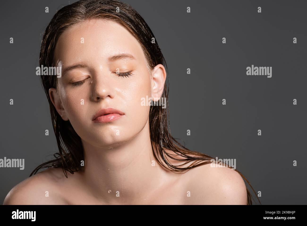 Bella donna con pelle bagnata chiudere gli occhi isolato sul grigio Foto Stock