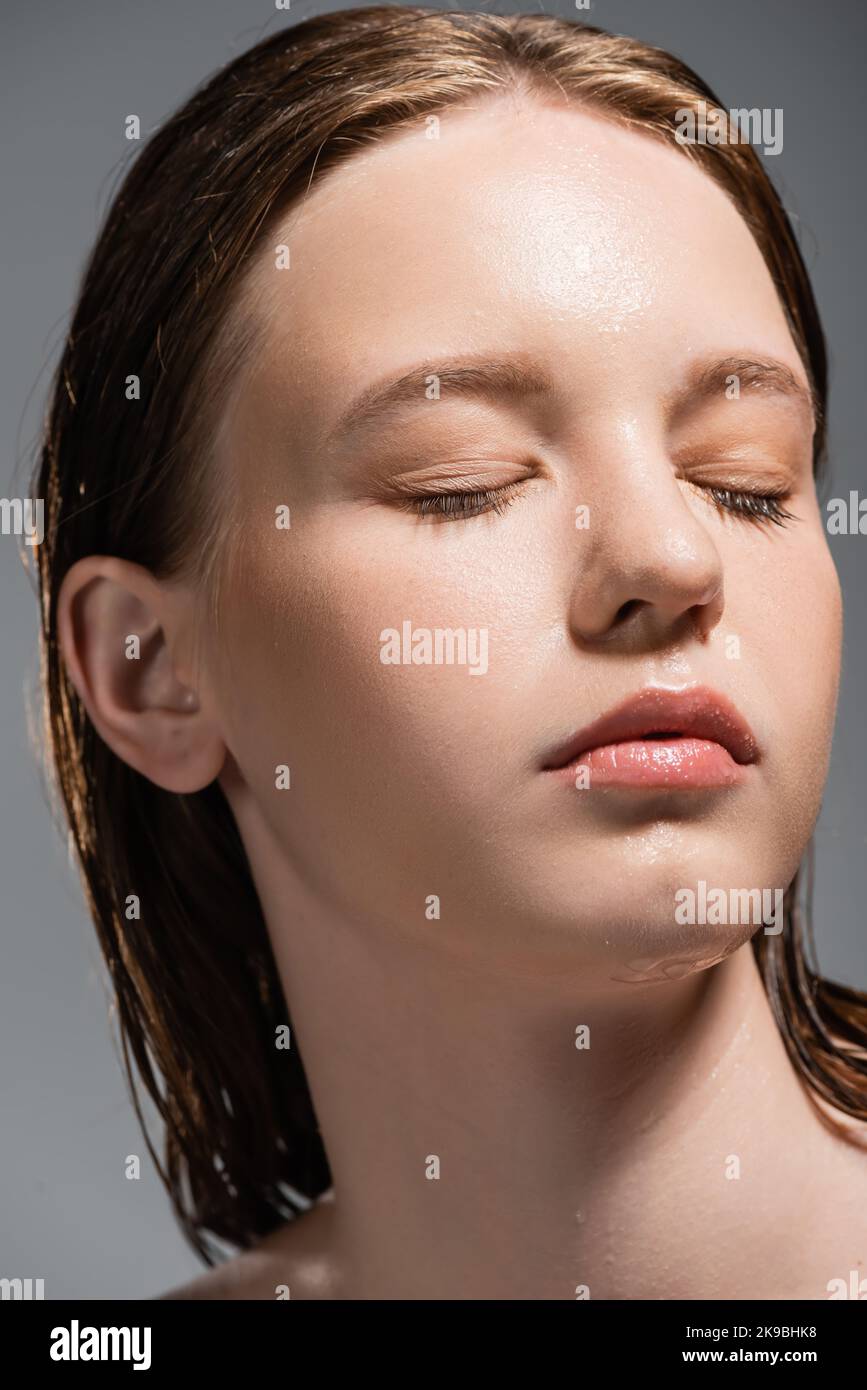 Ritratto di giovane donna con pelle bagnata occhi chiusi isolato su grigio Foto Stock