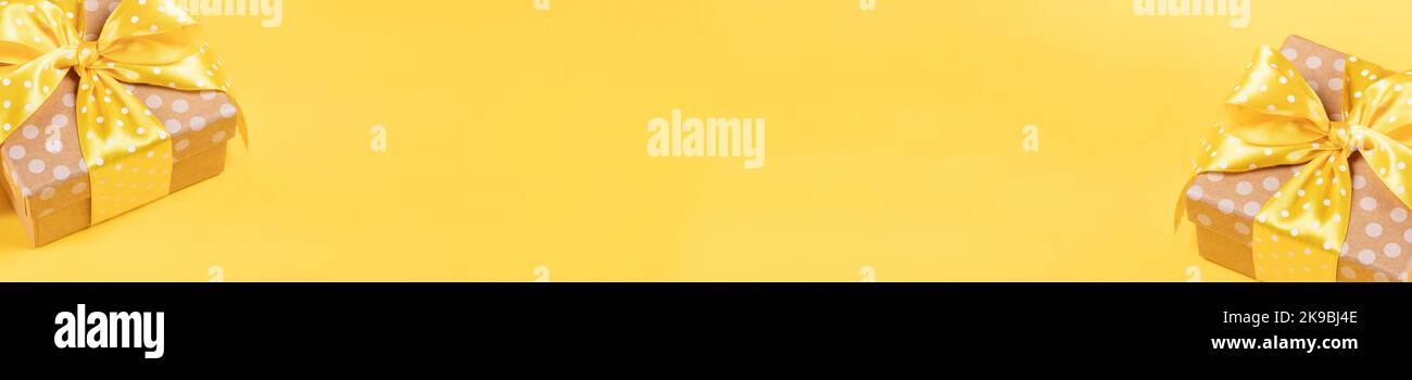 Banner giallo brillante per le vacanze con due scatole regalo avvolte punti di polka di carta artigianale decorati con nastri gialli e puntini di polka ad arco. Sfondo minimo Foto Stock