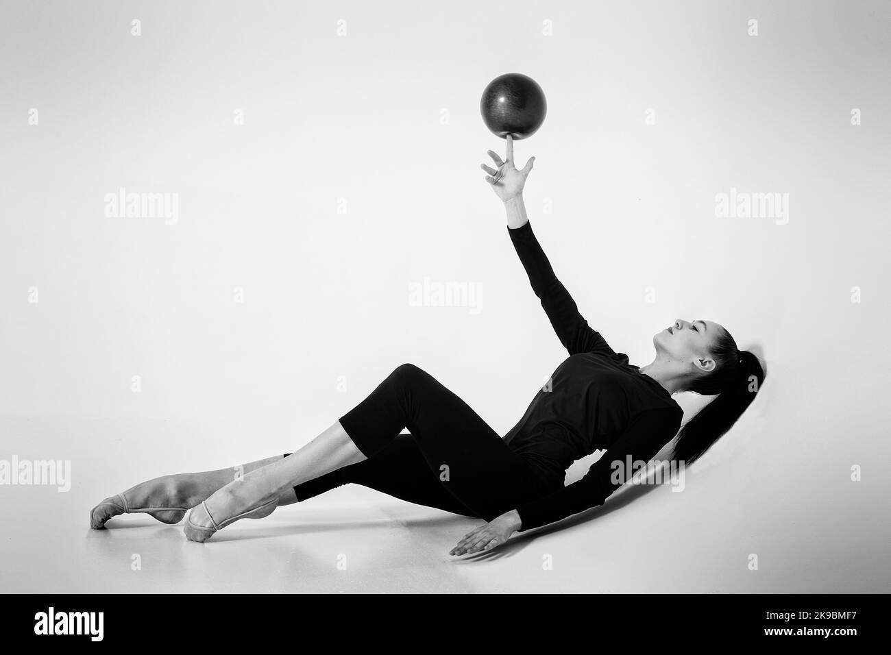 una ragazza di ginnastica ritmica in un bodysuit mostra stendersi sulla schiena girando una palla sul dito della mano sollevata Foto Stock