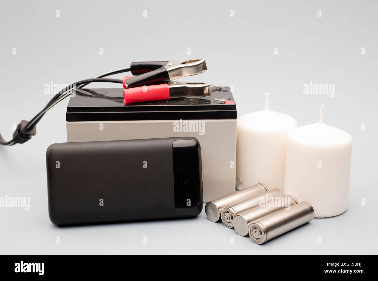 set di emergenza, power bank con batterie, candele bianche e batteria con bulloni di collegamento sfondo grigio Foto Stock