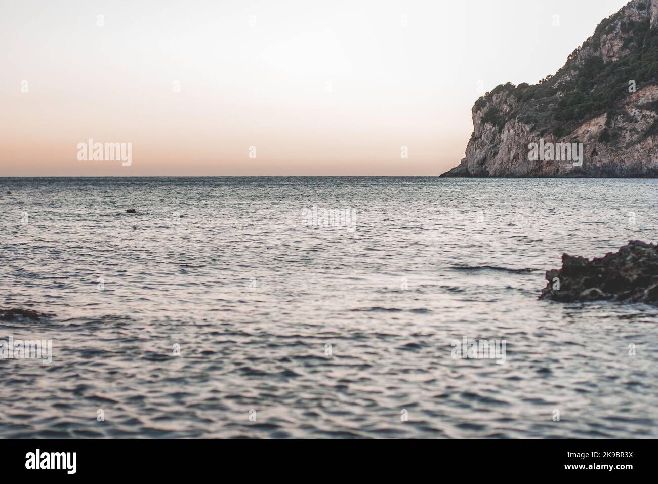 Corfù, Grecia. Bellissimo paesaggio con una roccia enorme in acqua al tramonto. Foto Stock