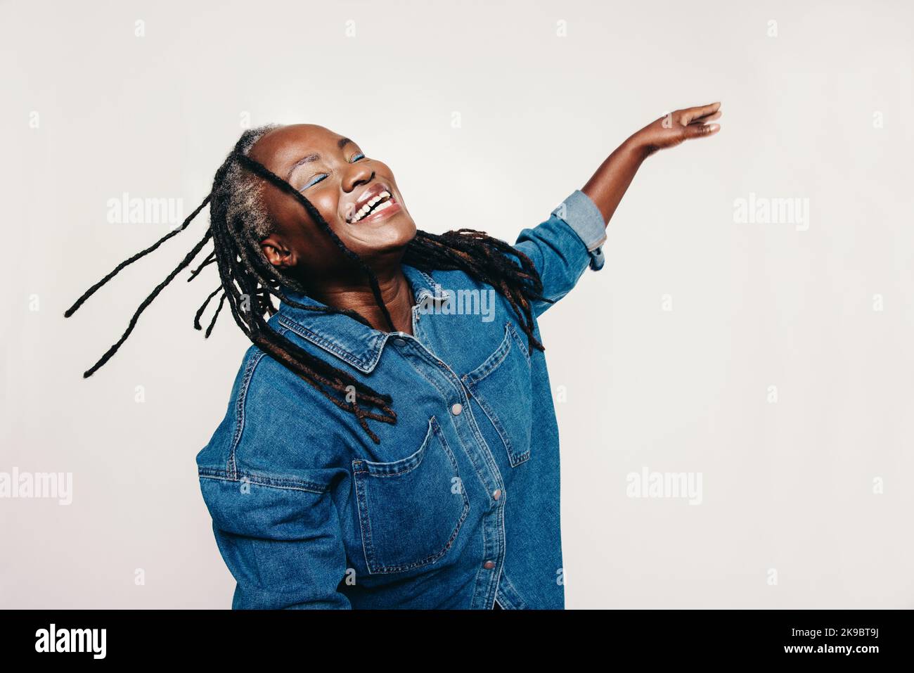Felicità in studio. Donna matura con greggi ridendo con gli occhi chiusi e le braccia distese. Donna gioiosa di mezza età che indossa un deni Foto Stock