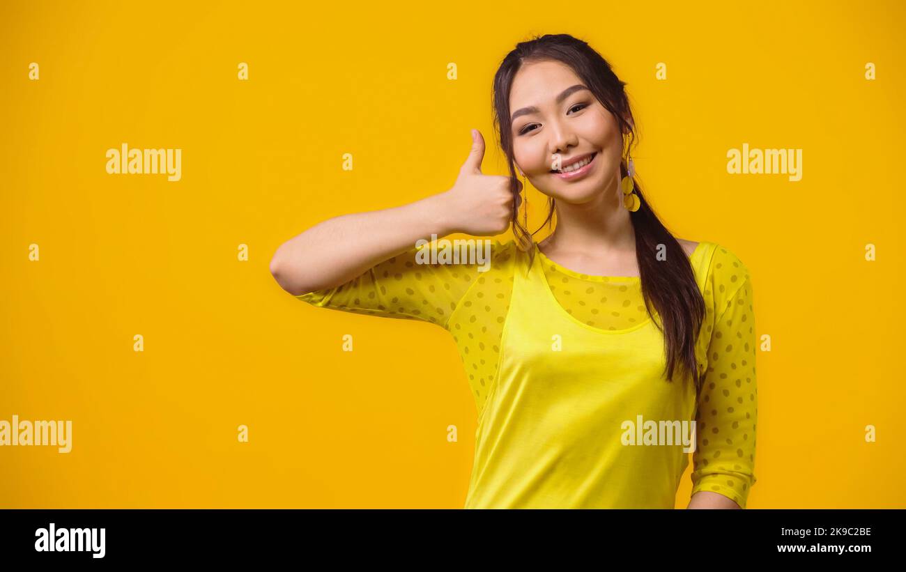 giovane donna asiatica positiva che mostra pollice isolato su giallo Foto Stock