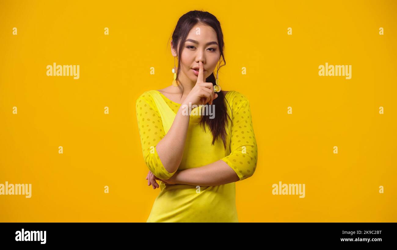 giovane donna asiatica che mostra un segno di fush e sorridente isolato su giallo Foto Stock