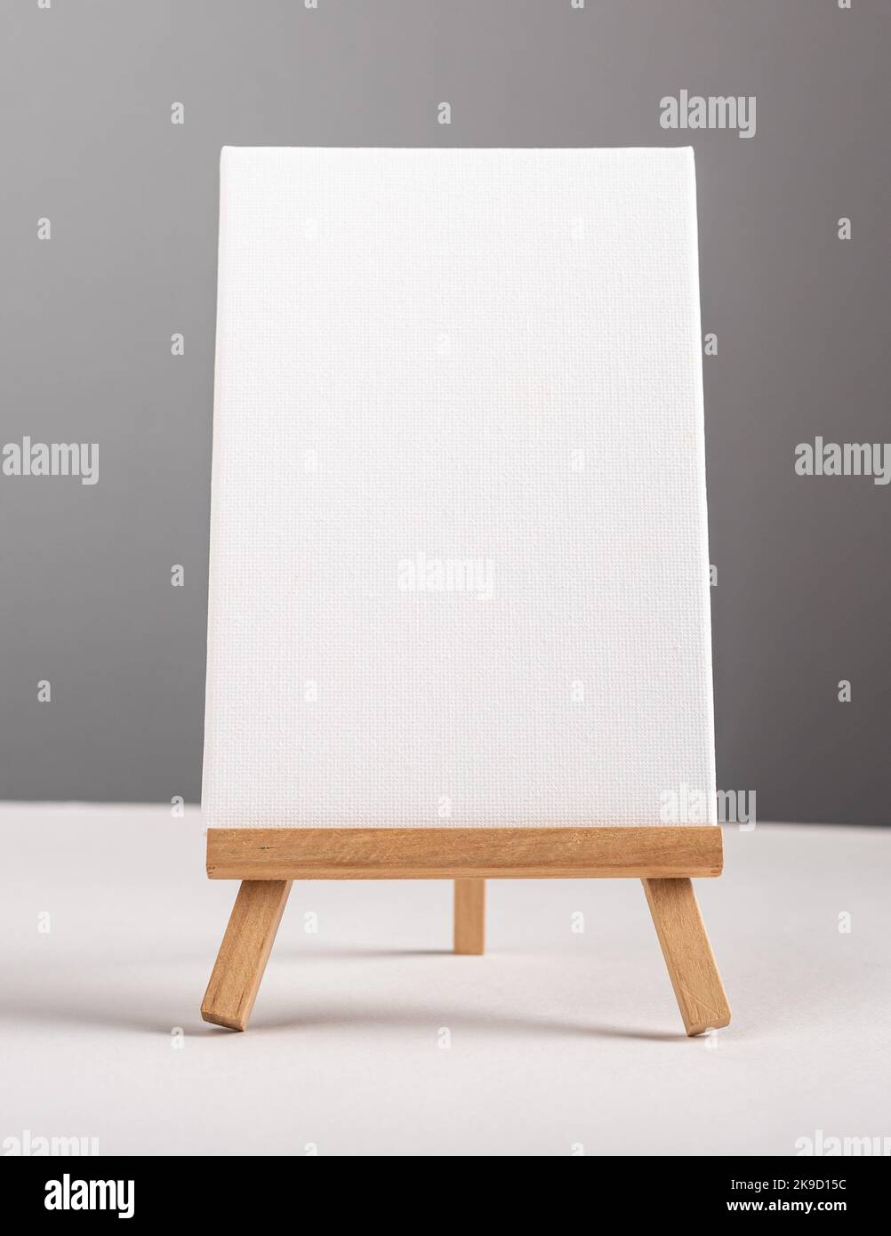 Verticale vuoto bianco canvas mock up in piedi su mini treppiede di legno sulla scrivania. Foto di alta qualità Foto Stock