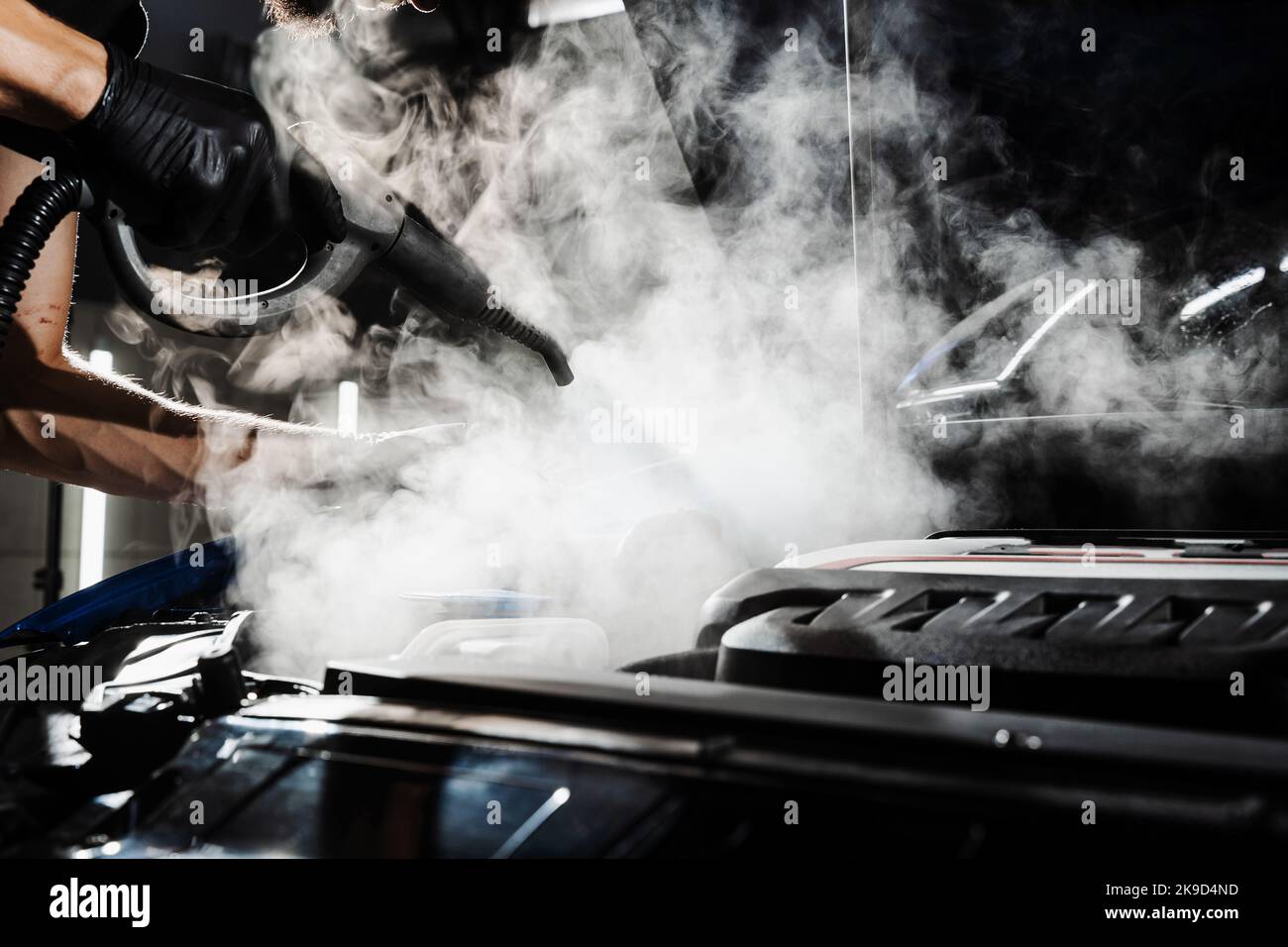 Processo di pulizia a vapore del motore dell'auto da polvere e sporcizia. Lavaggio a vapore del motore di auto nei dettagli del servizio auto Foto Stock