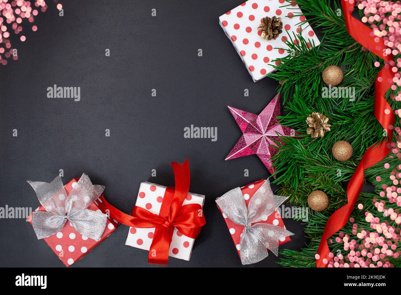 Scatole regalo con archi, rami di abete, stella, nastro e bokeh su sfondo nero. Natale, Capodanno. Spazio di copia Foto Stock