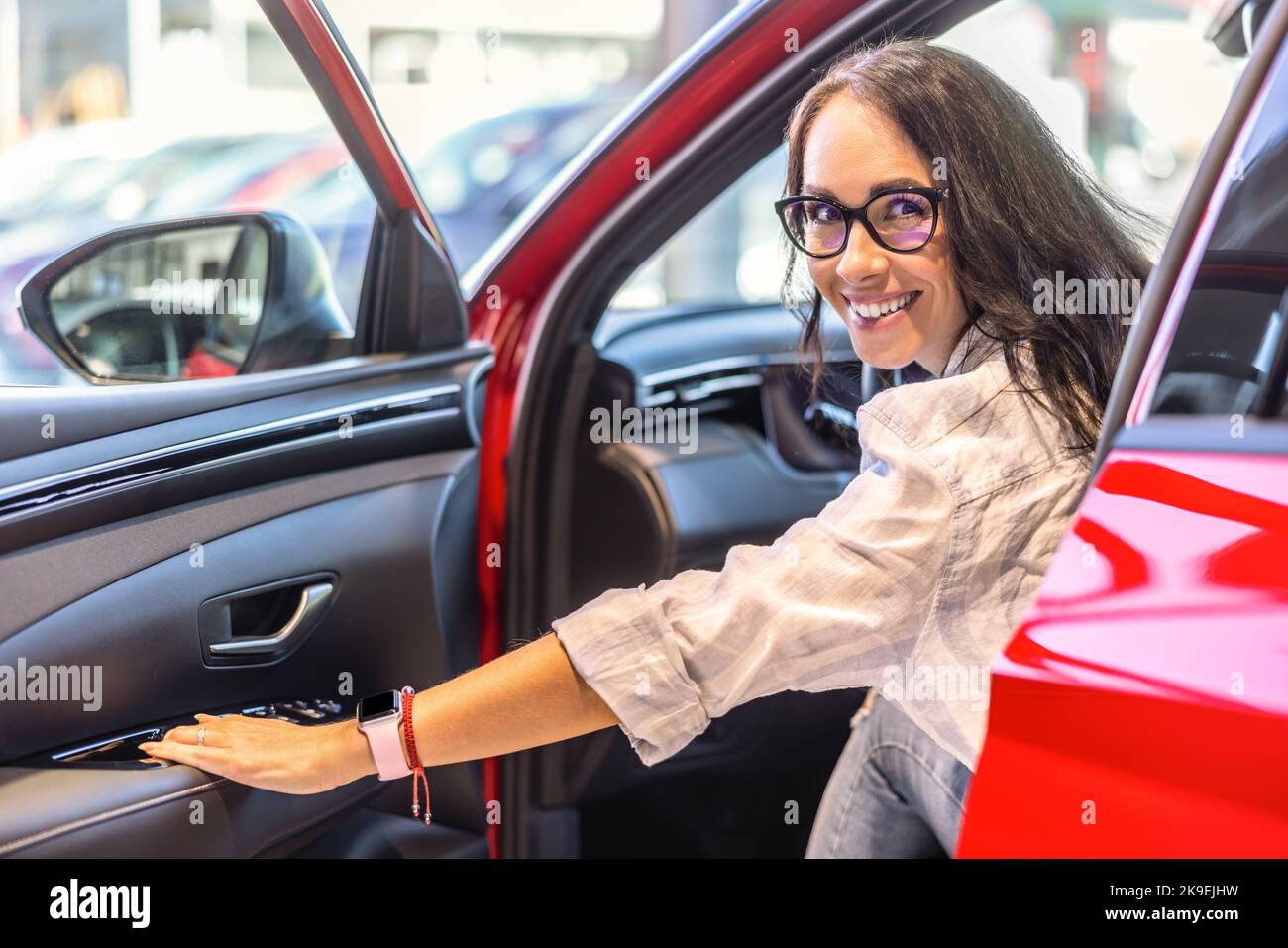 Buona donna di vendita dell'automobile che osserva seduto in una nuova automobile e che guarda la macchina fotografica. Foto Stock