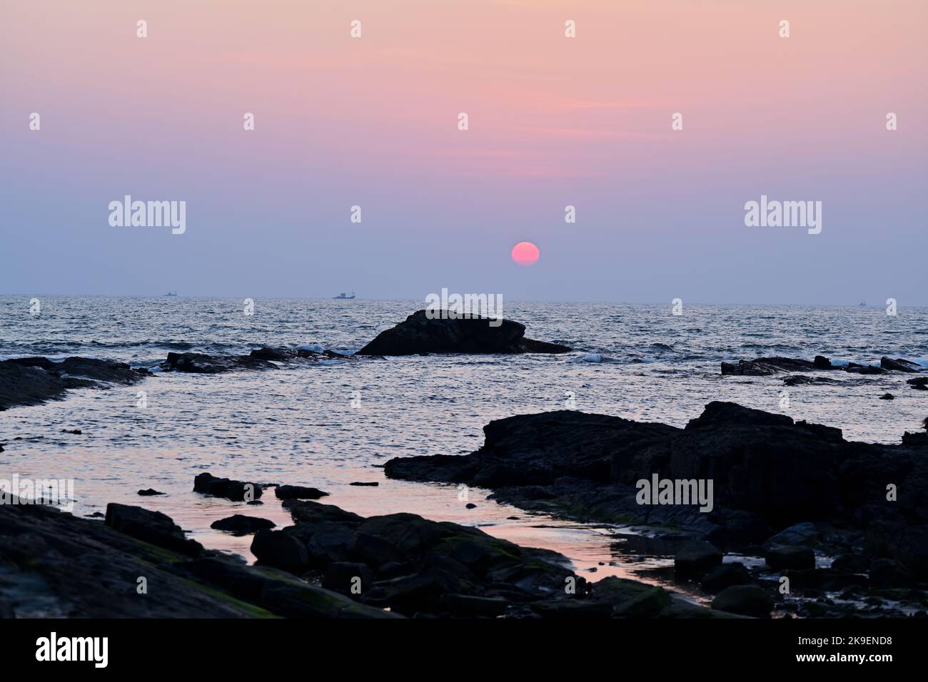 Goa | roccia nera in mezzo al mare che testimonia il tramonto Foto Stock