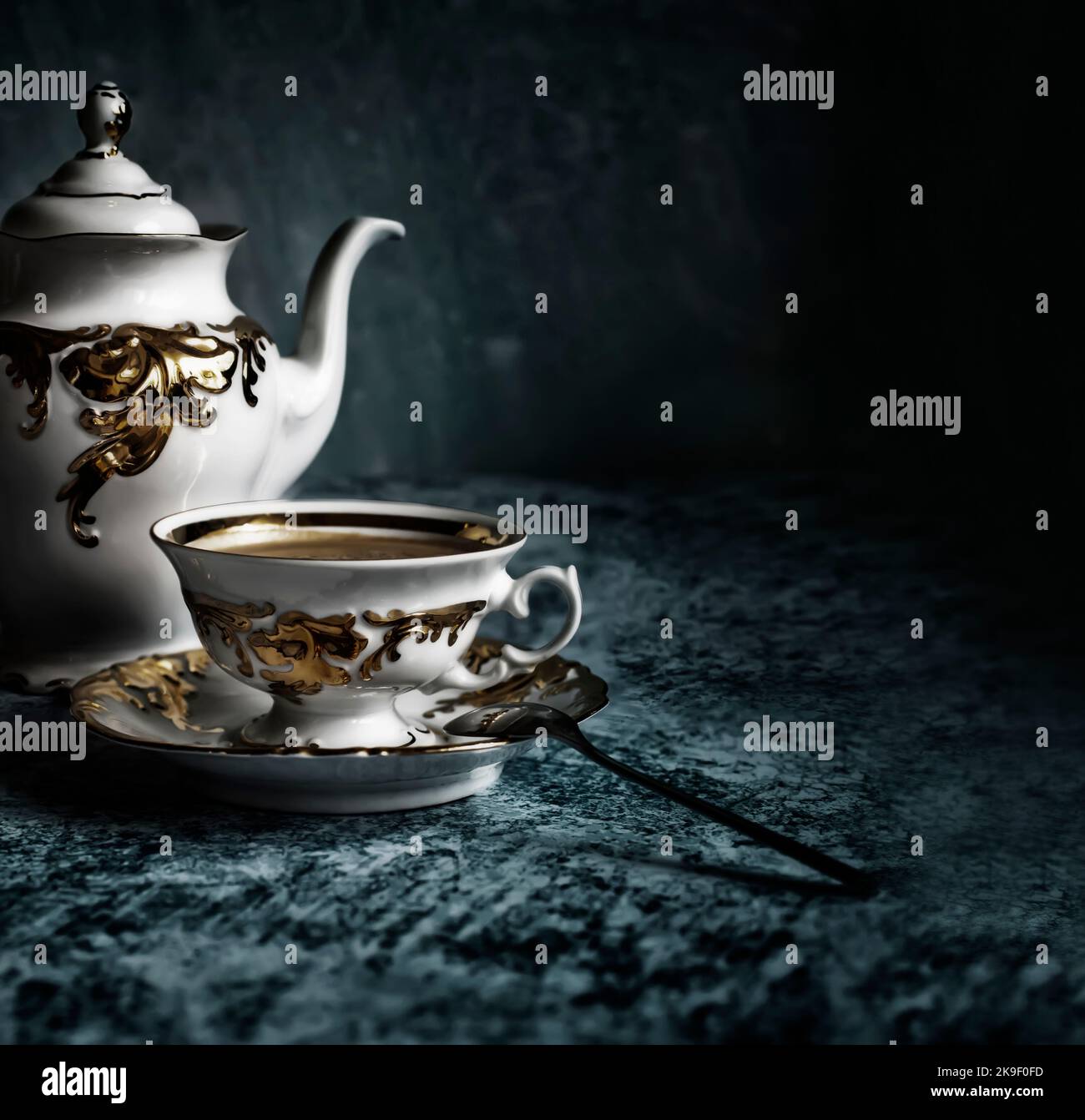 Raffinata tazza da caffè bianca e dorata su sfondo blu astratto. Caffè con un'appetitosa schiuma dorata. Foto Stock