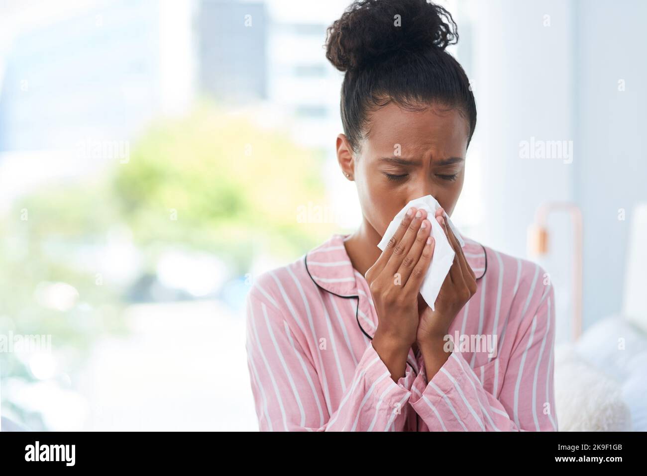 Questa mattina mi sento terribile: Una giovane donna ammalata che soffia il naso con un fazzoletto a casa. Foto Stock