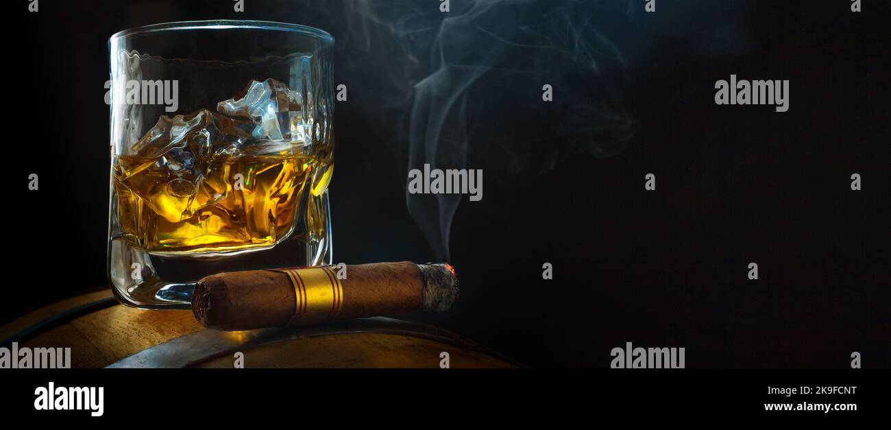 un bicchiere di whisky con ghiaccio su un barile di quercia, un sigaro cubano fumante in un'atmosfera fumosa di un bar notturno. Uomo banner idea club. Copia spazio per il testo Foto Stock