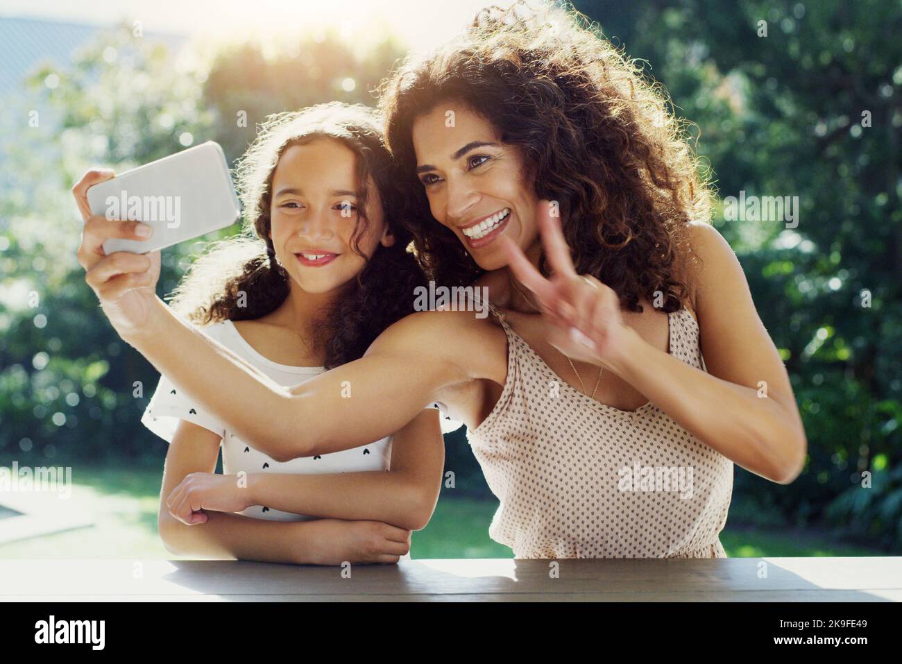 Mettiti in posa: Una giovane madre e sua figlia prendono selfie insieme al parco durante il giorno. Foto Stock