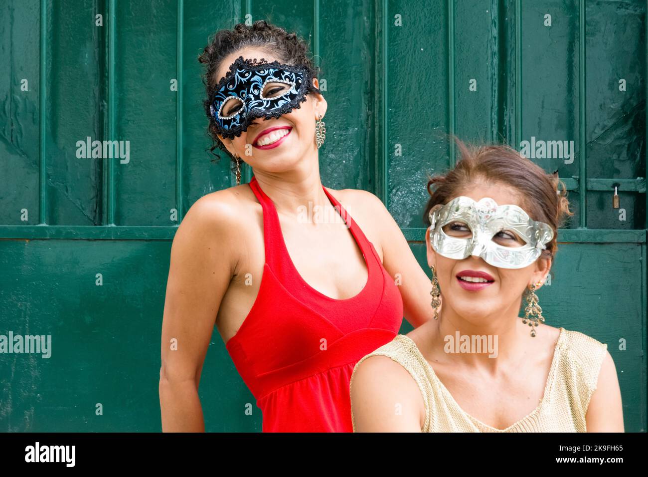 Due ragazze che indossano la maschera di carnevale nei vestiti estivi chiari stanno sedendosi contro una porta di colore verde. Ragazze di città lontano dalla capitale. Foto Stock