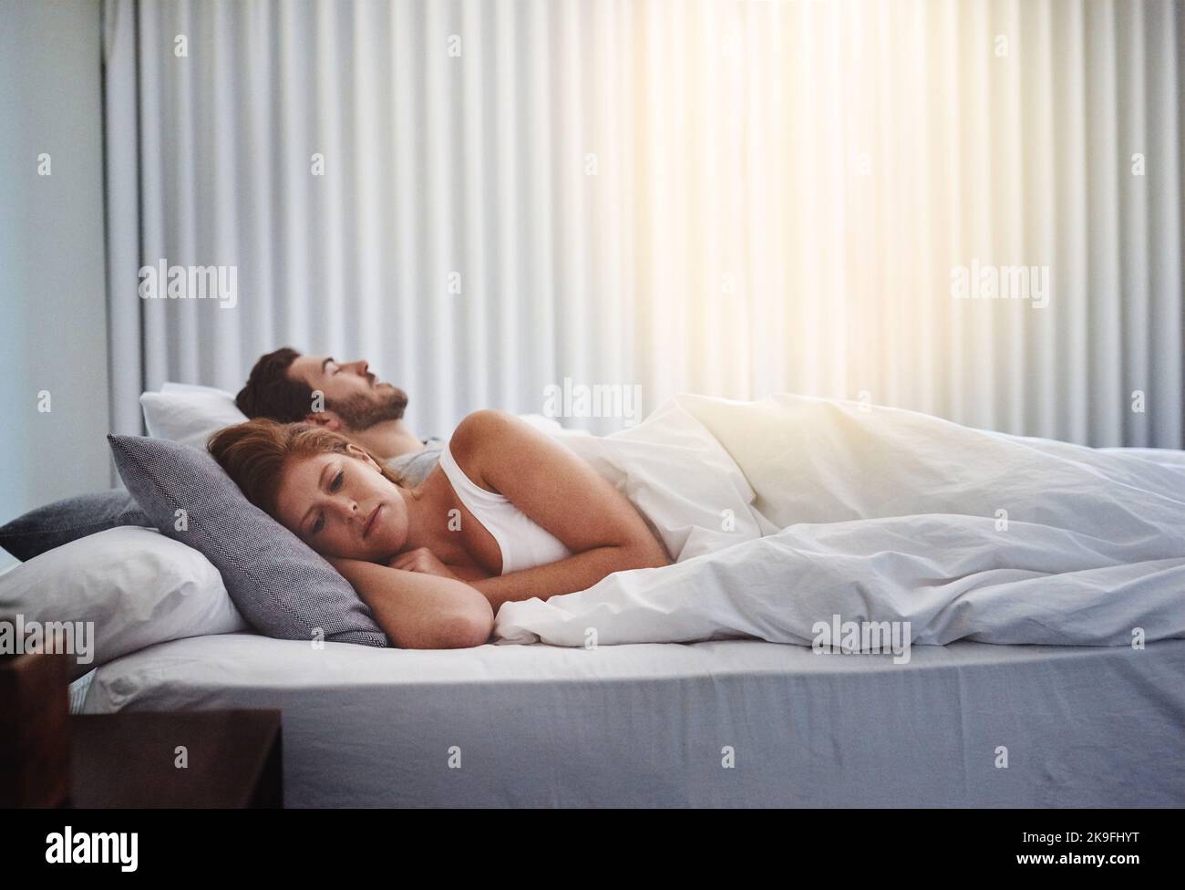 Non riesco a dormire con tanti stress sulla mia mente: Una donna che guarda turbata mentre suo marito dorme accanto a lei a casa. Foto Stock