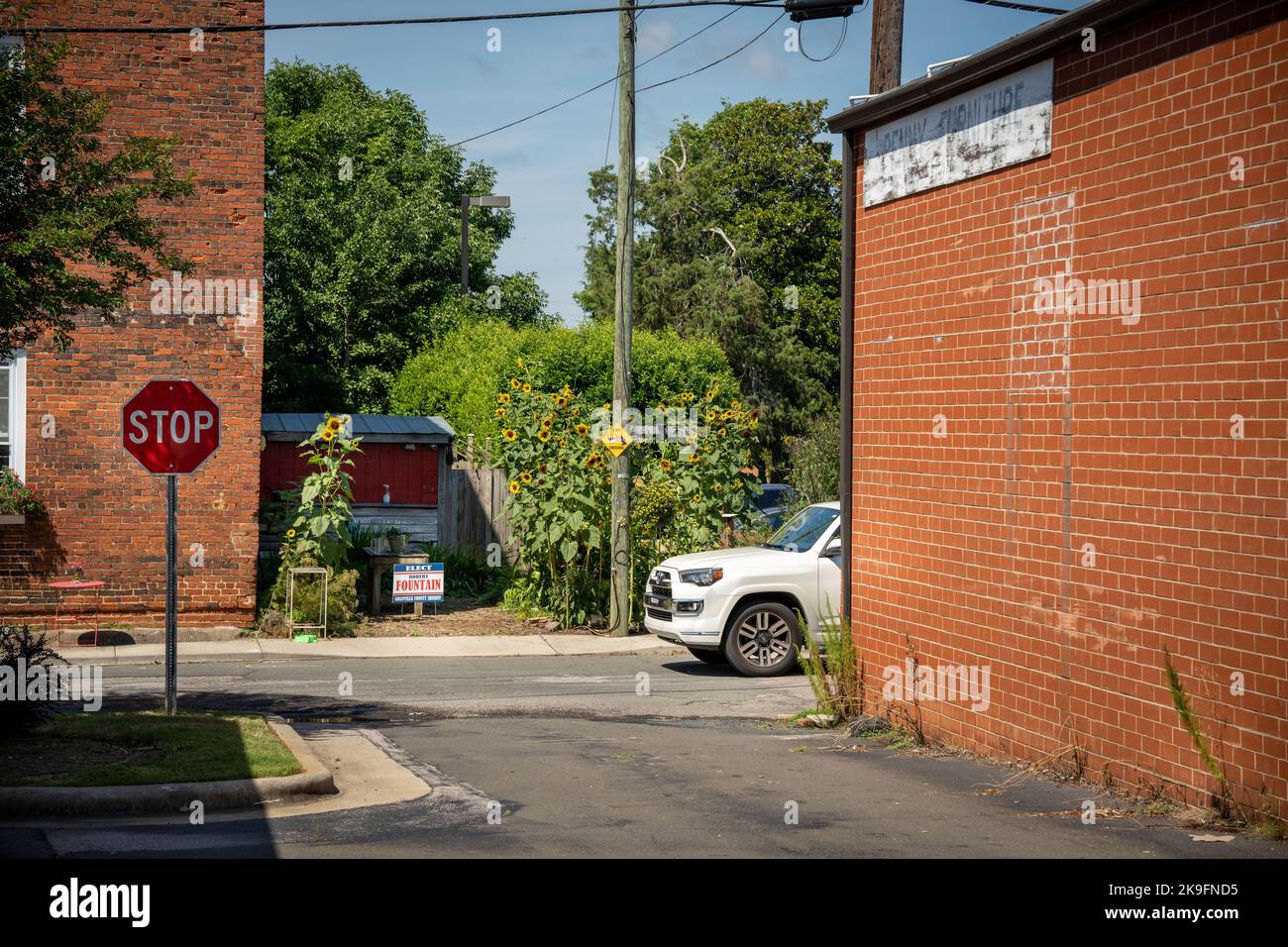 Il SUV bianco guida lungo una strada americana, superando un segnale di stop e girasoli Foto Stock