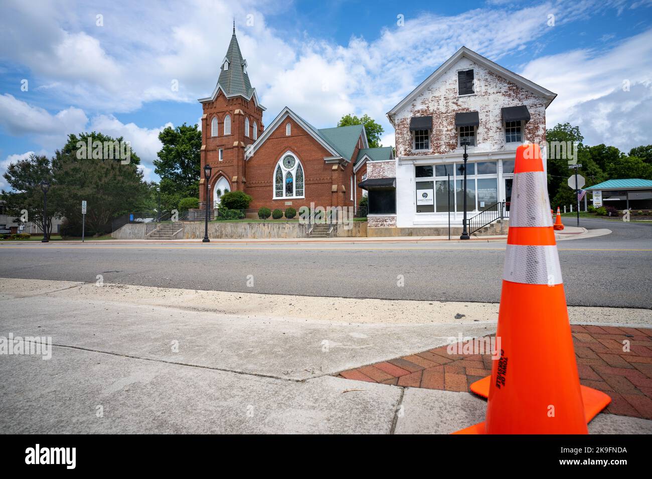 Chiesa accanto a una casa in vendita su una strada con un pilone arancione Foto Stock