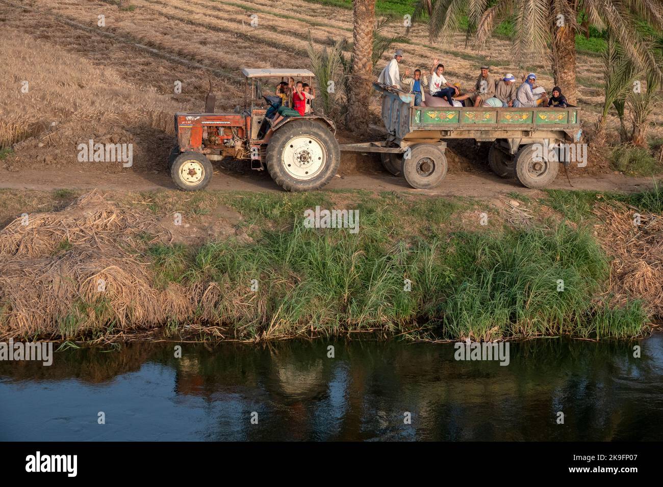I lavoratori agricoli che sventolano da un trattore e da un rimorchio sulle rive del fiume Nilo, Egitto, Africa Foto Stock
