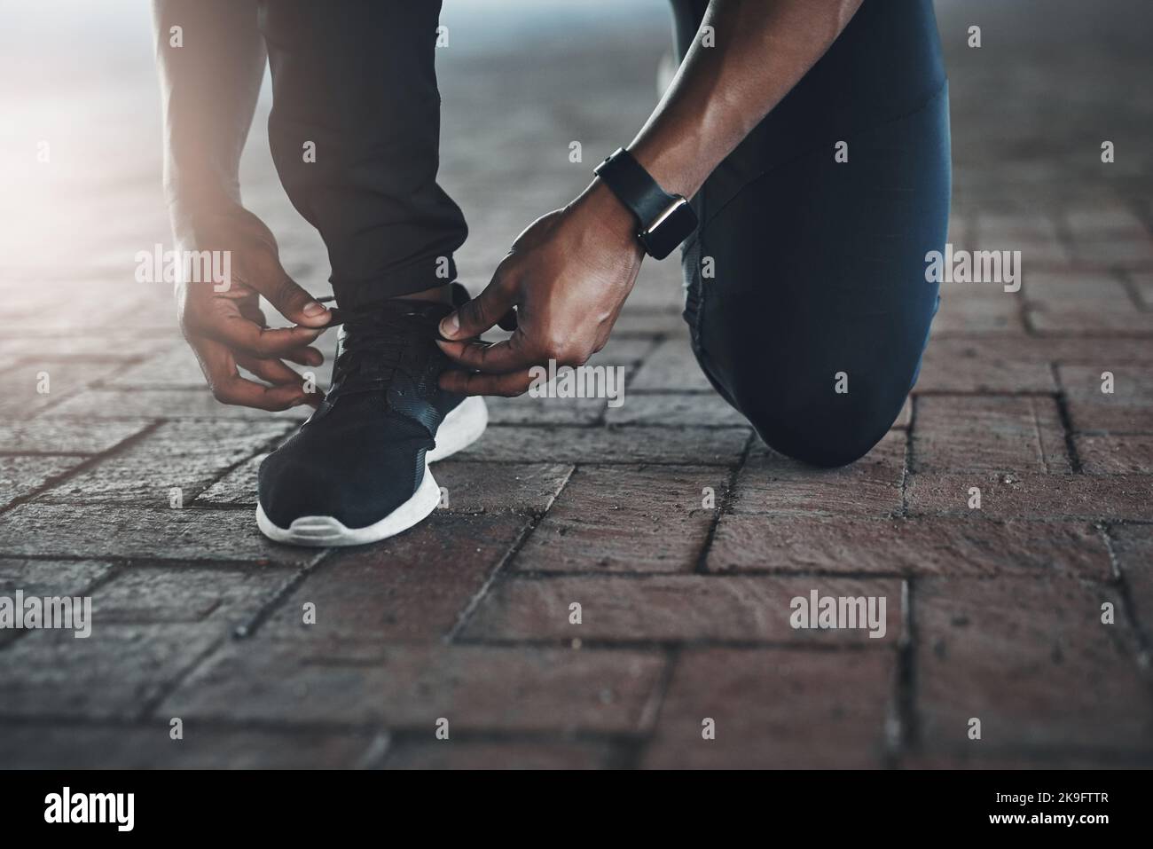 Assicurandosi che i suoi lacci siano stretti. Un giovane uomo irriconoscibile che legava i suoi lacci mentre esercitandosi fuori. Foto Stock