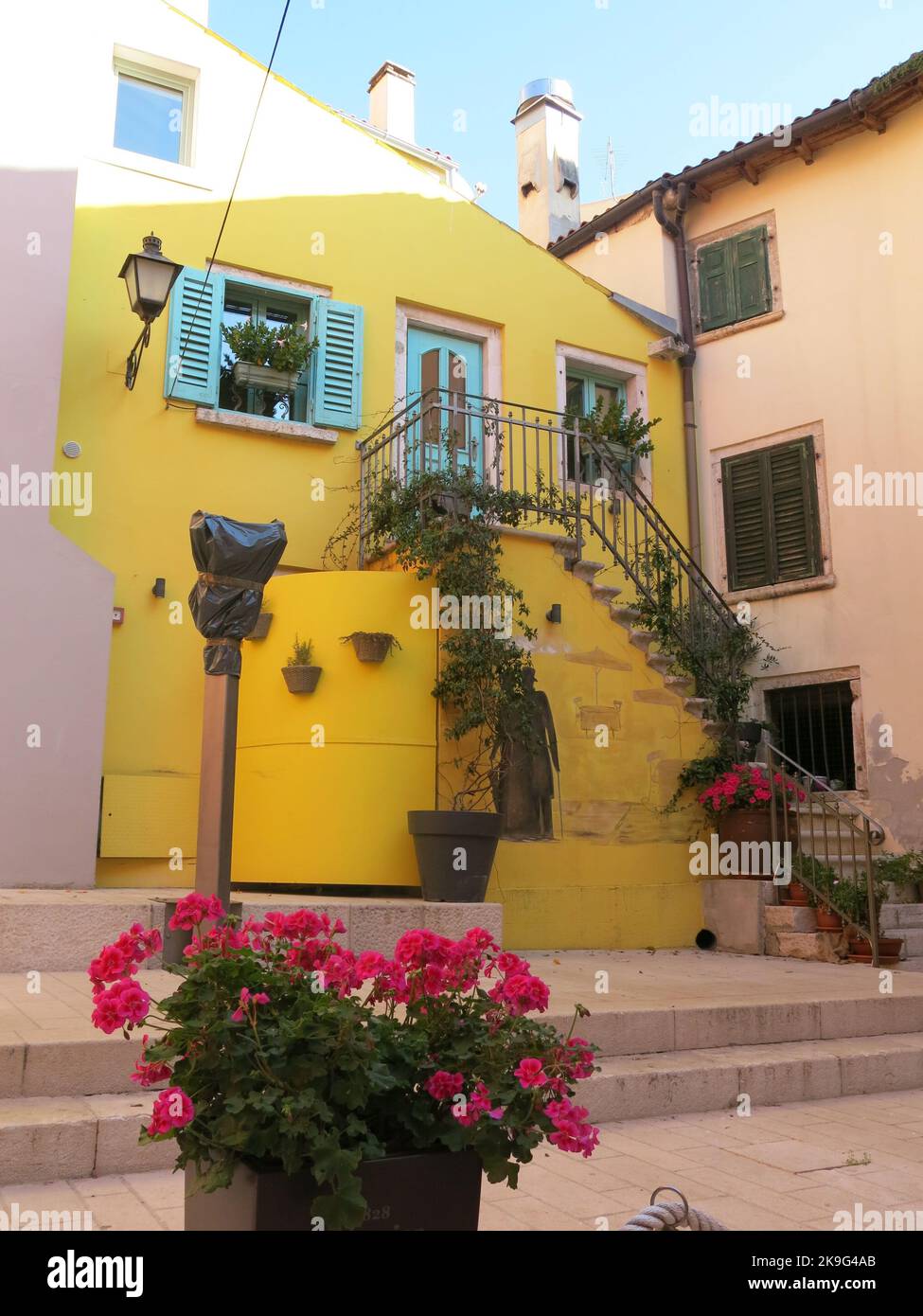 La graziosa cittadina di Rovigno: Una casa di colore giallo, con persiane verdi, figure nere stencil sul muro e gerani rossi in una pentola. Foto Stock