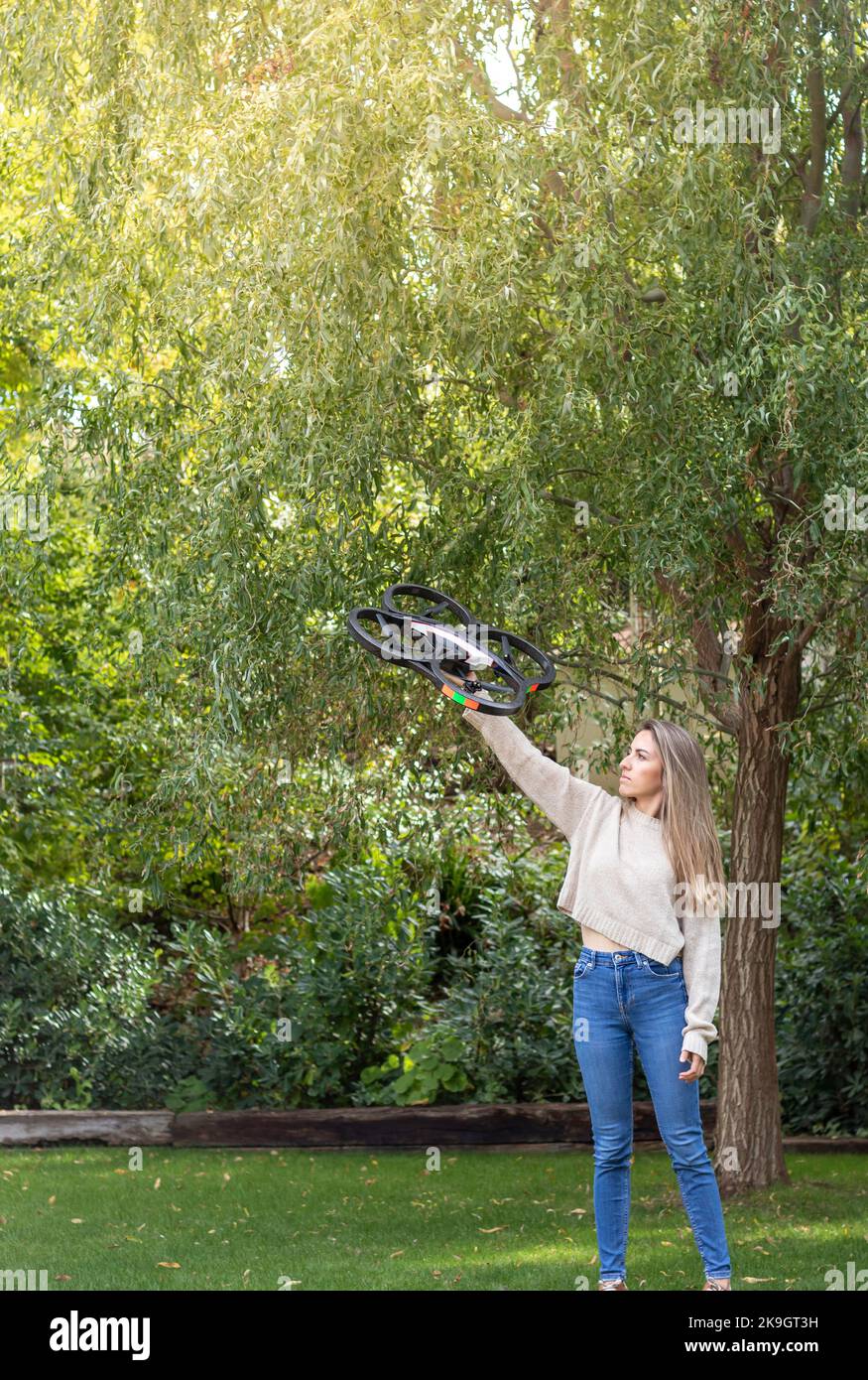 Ritratto a tutta lunghezza lontano di una giovane ragazza che alza il suo nuovo enorme drone nel giardino accanto agli alberi verdi Foto Stock