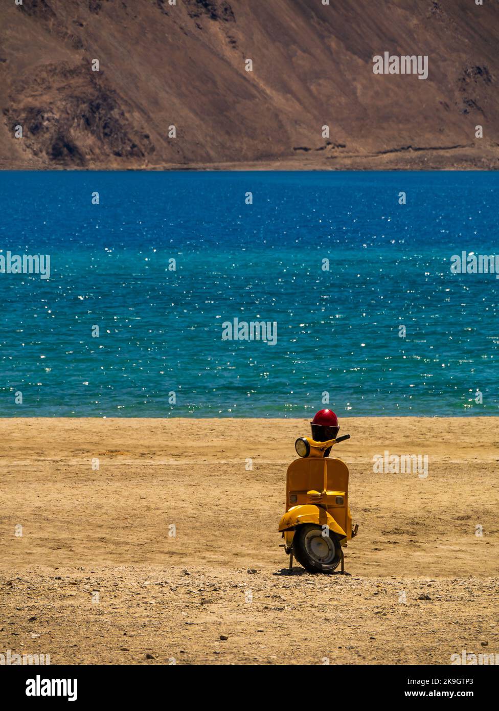 Ladakh, India - 26 giugno 2022 : scooter giallo al lago Pangong, il lago di acqua salata più alto del mondo in una posizione blu in netto contrasto con le aride montagne Foto Stock