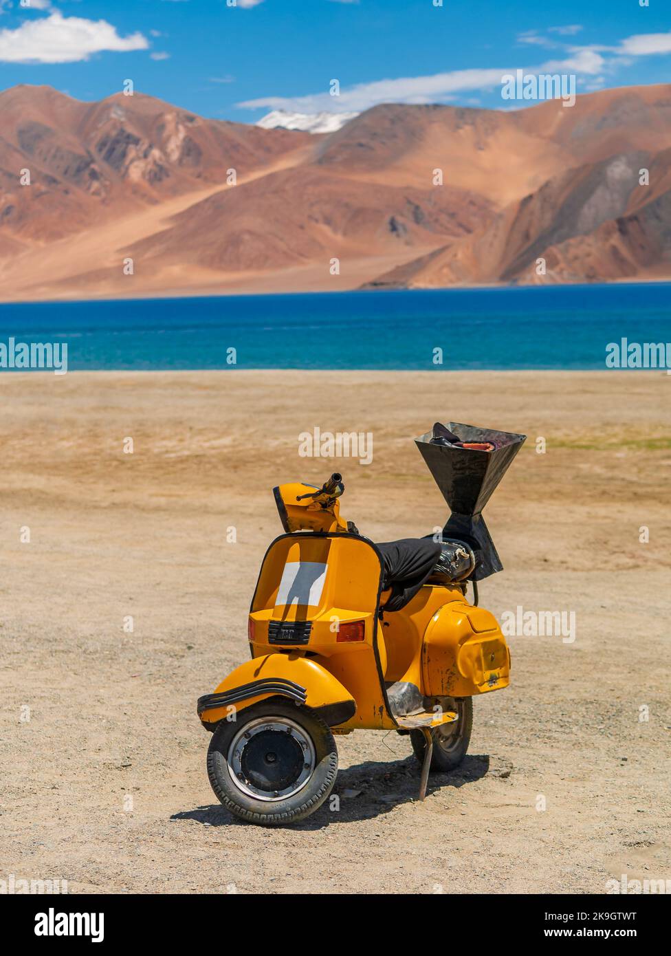 Ladakh, India - 26 giugno 2022 : scooter giallo al lago Pangong, il lago di acqua salata più alto del mondo in una posizione blu in netto contrasto con le aride montagne Foto Stock