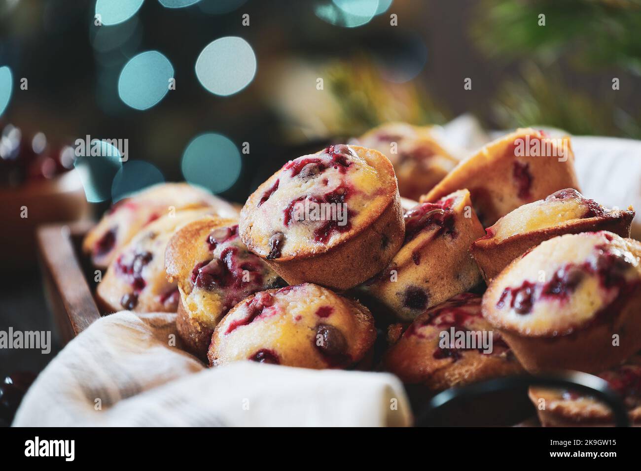 Muffin ai mirtilli rossi in un vassoio di legno con bokeh all'albero di Natale e frutti di bosco freschi sullo sfondo. Messa a fuoco estremamente selettiva con sfondo sfocato. Foto Stock