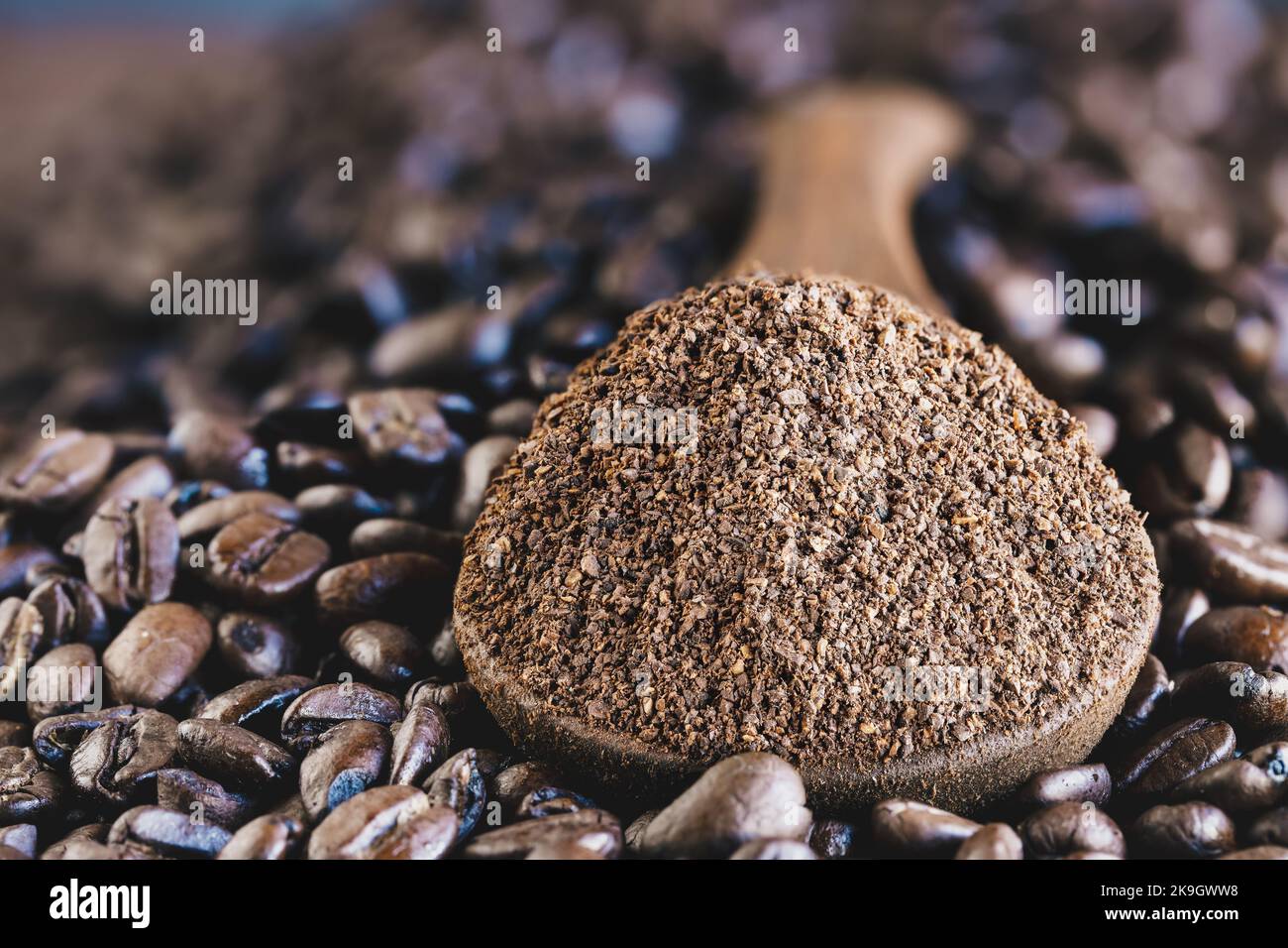 Estratto di un cucchiaio di legno di caffè macinato su uno strato di chicchi di caffè appena tostati. Messa a fuoco estremamente selettiva al centro con primo piano sfocato A. Foto Stock