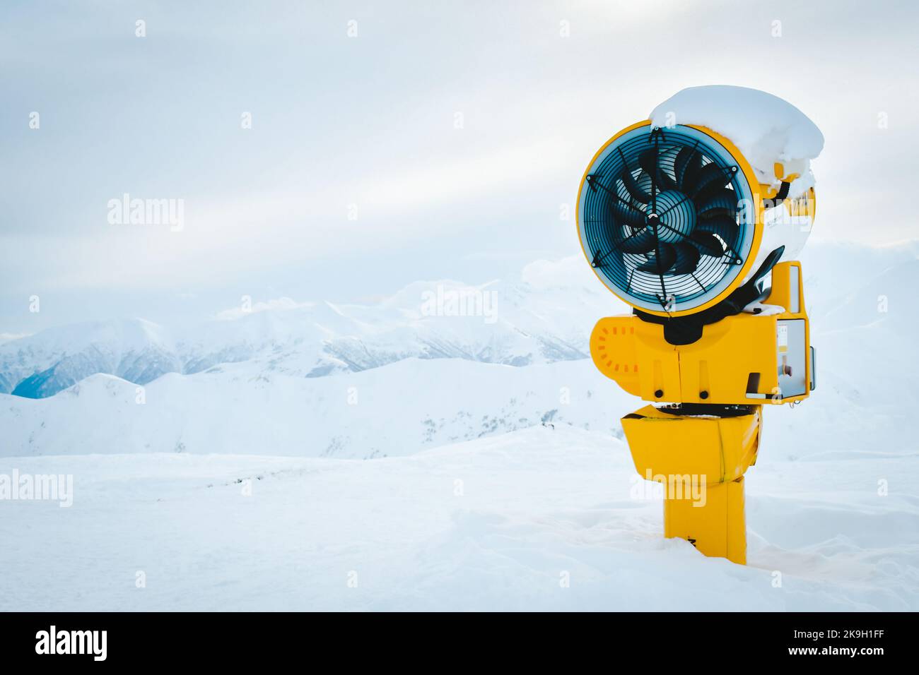 Cannone di neve gialla sotto la neve nella stazione sciistica di Gudauri in montagne innevate dopo una fresca caduta di neve. Buona situazione di neve e finta tecnologia neve Foto Stock