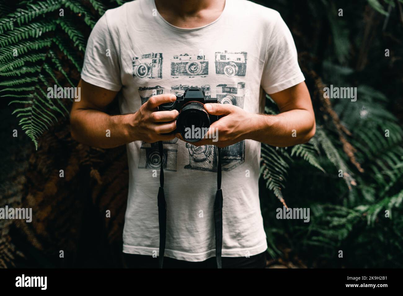 ragazzo caucasico in una t-shirt bianca e cartoon di vecchie macchine fotografiche che mostra una fotocamera fotografica pronta a scattare una foto nella foresta su donut island, nuovo Foto Stock
