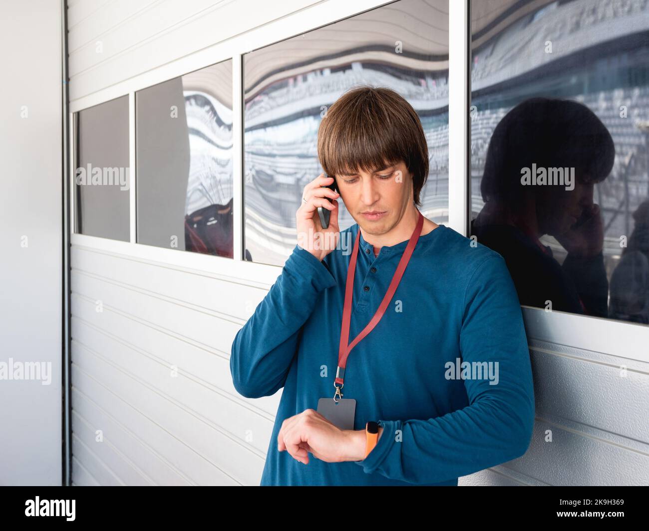 L'uomo con badge sul nastro rosso parla da smartphone e guarda sul wristwatch sulla pit lane all'autodromo. Corse di auto sportive. Competizione sportiva Foto Stock
