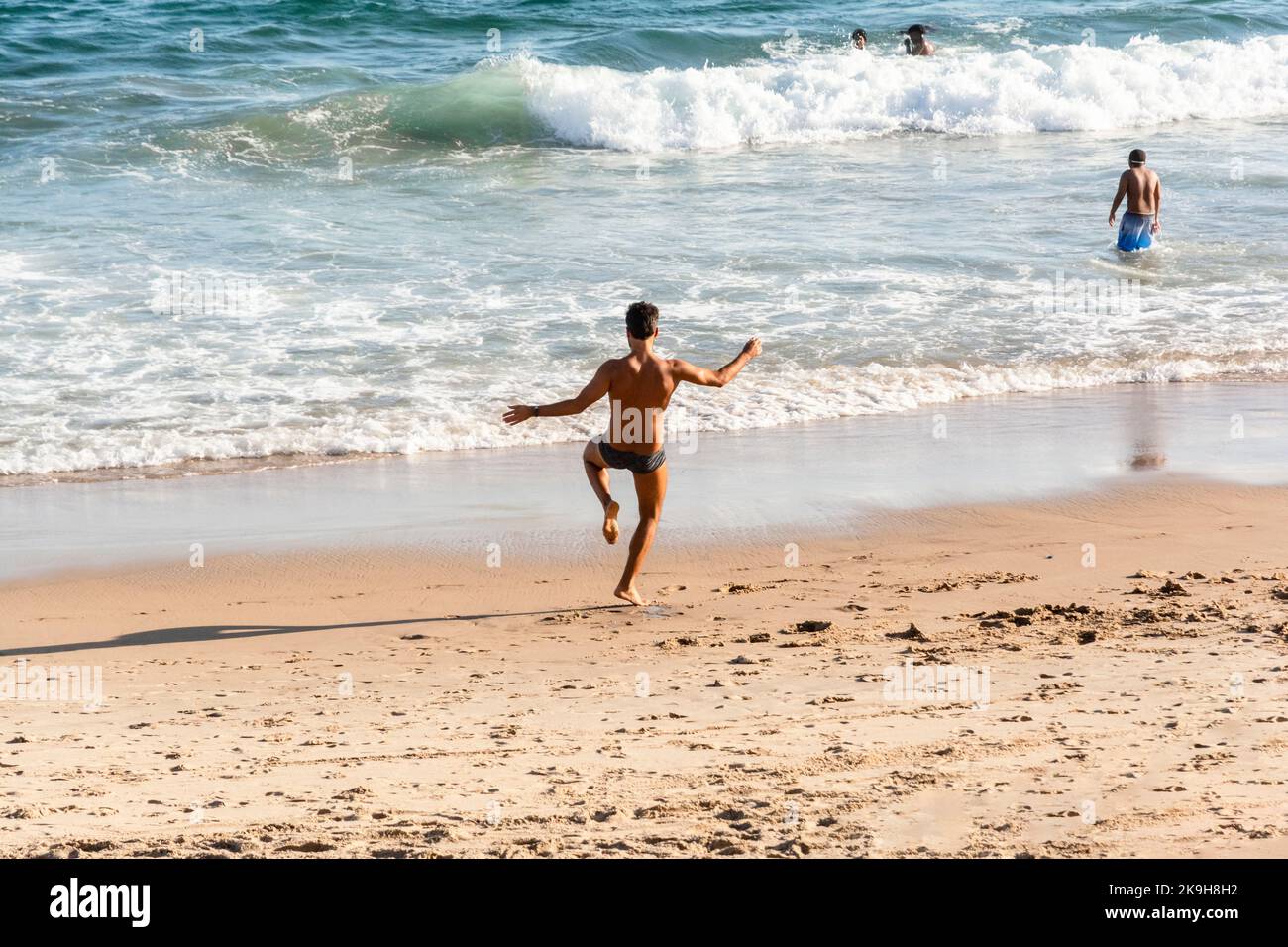 Salvador, Bahia, Brasile - 22 ottobre 2022: Un uomo fa esercizi di yoga sulla sabbia di Farol da barra spiaggia a Salvador, Brasile, mentre altre persone a piedi Foto Stock
