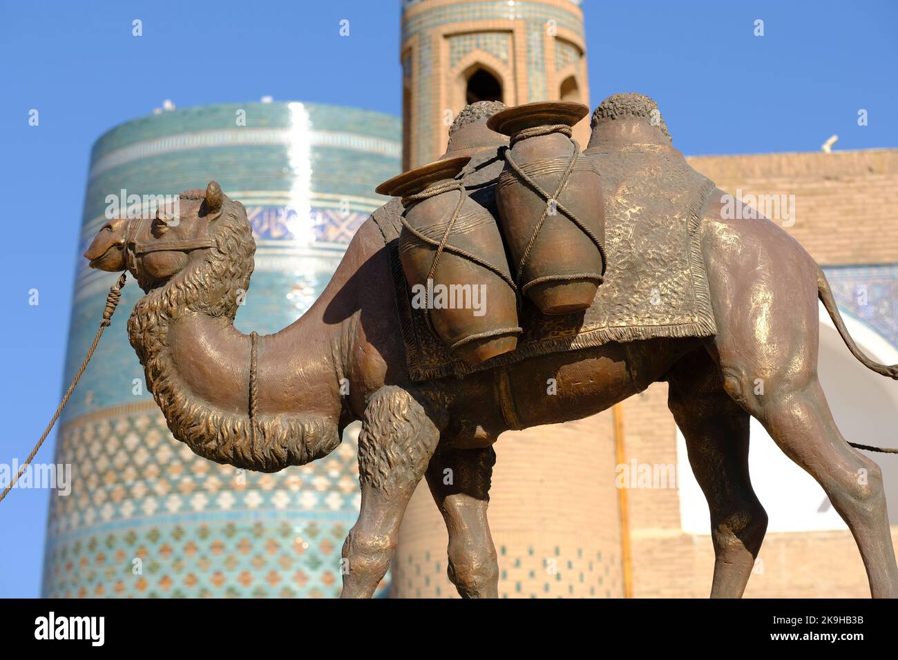 Khiva Uzbekistan - Camel figura monumento alle antiche strade della Seta presso il sito IInchon Qala UNESCO con il minareto Kalta Minar sullo sfondo Foto Stock