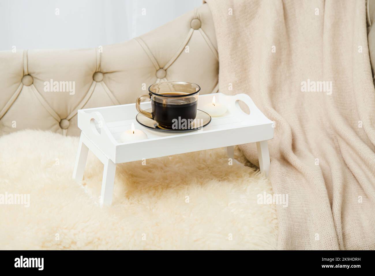 Grazioso vassoio di legno bianco per la colazione con gambe sul letto di casa con una tazza di caffè caldo del mattino, candele bruciate. Set di sistemazione autunnale con plaid di lana morbida. Foto Stock