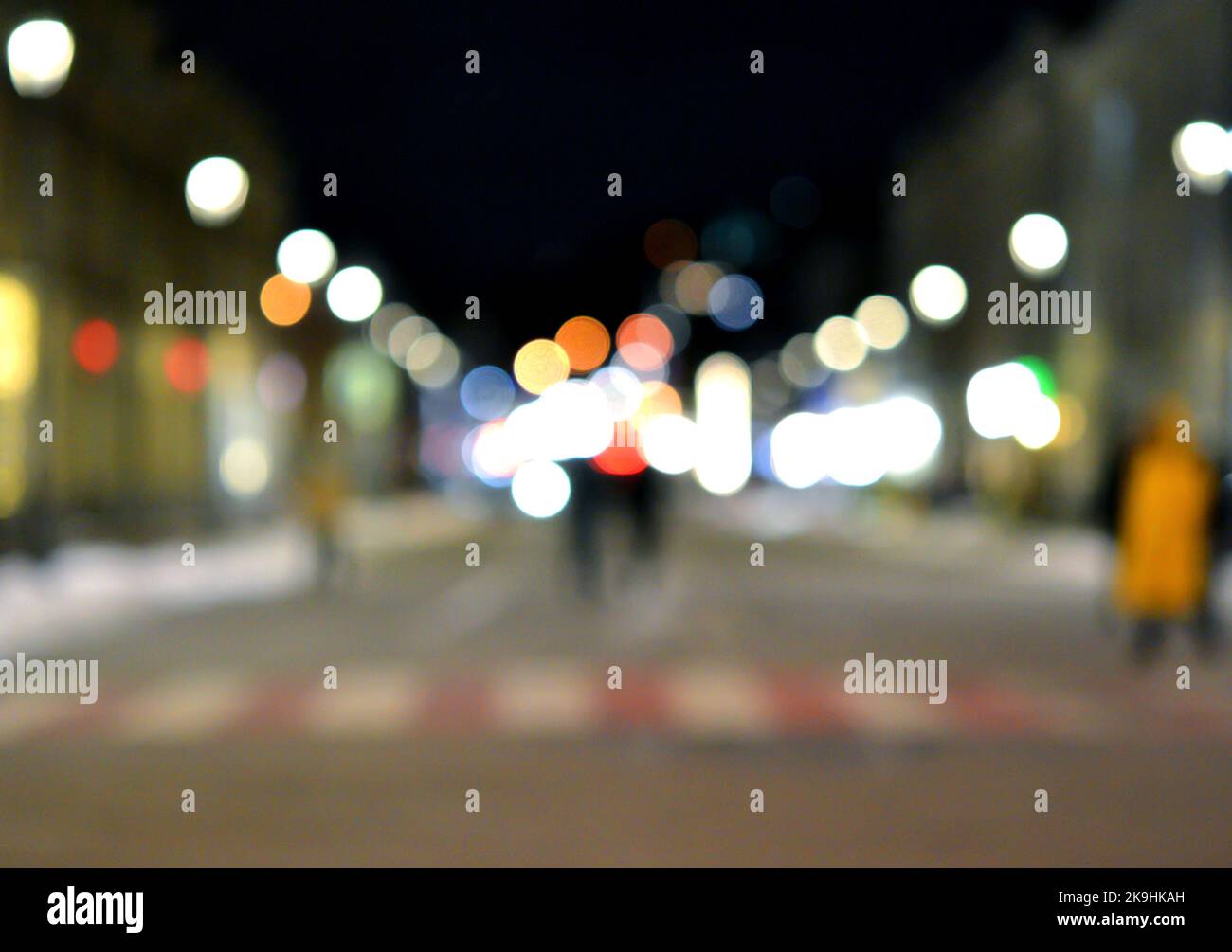 Sfondo sfocato. Notte città. Silhouette sfocata degli edifici, macchie bokeh di lanterne luminose, silhouette sfocate di persone che camminano per strada la sera. Piazza della città, cielo nero notte Foto Stock