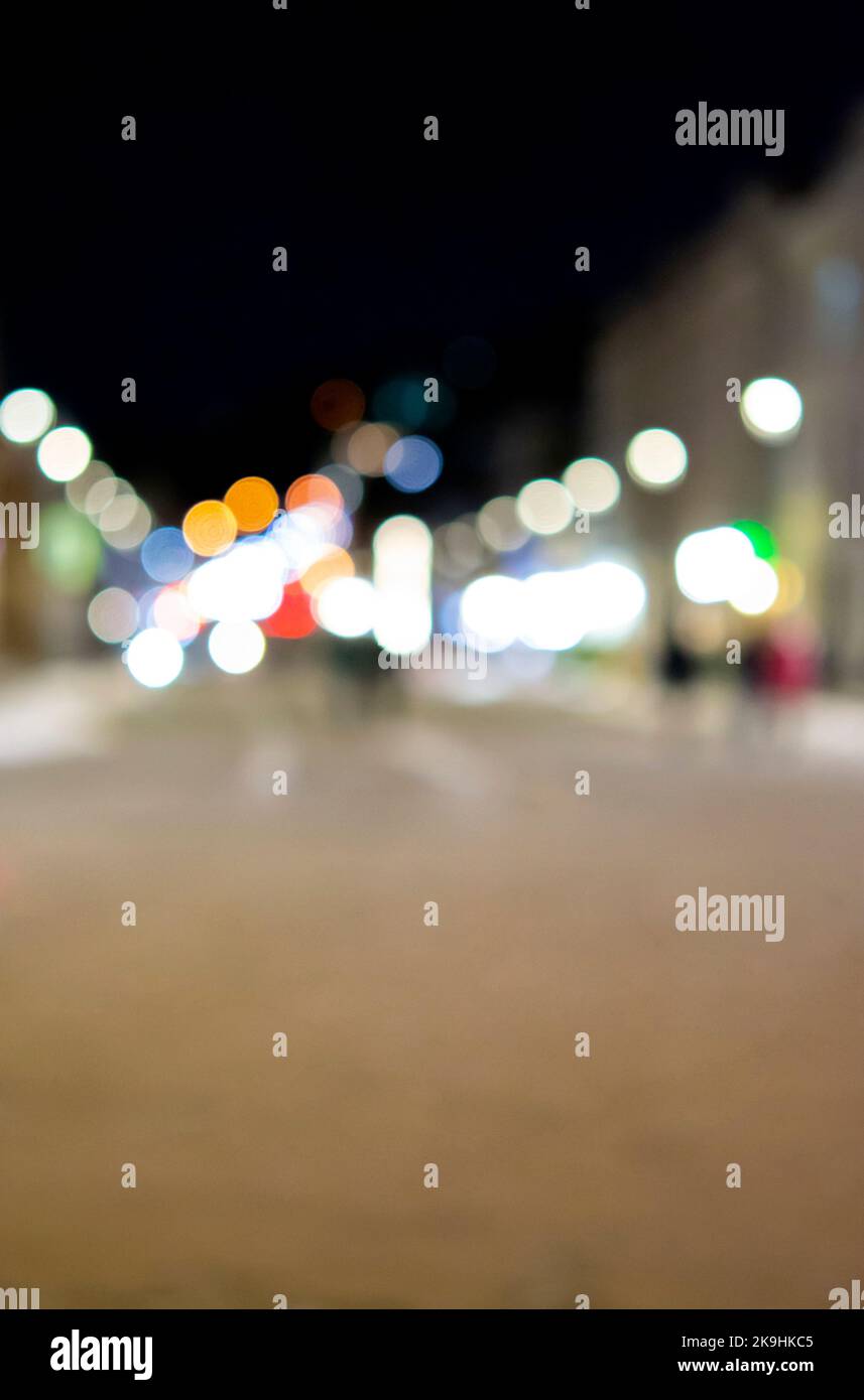 Sfondo sfocato. Notte città. Silhouette sfocata degli edifici, macchie bokeh di lanterne luminose, silhouette sfocate di persone che camminano per strada la sera. Piazza della città, cielo nero notte Foto Stock