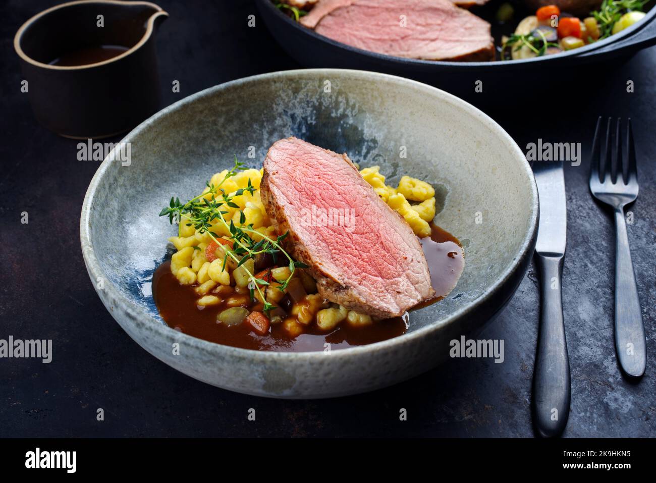 Fettine di vitello arrosto Tafelspitz con spaetzle svevo servite con salsa di birra scura come primo piano in una ciotola e una pentola di design Foto Stock