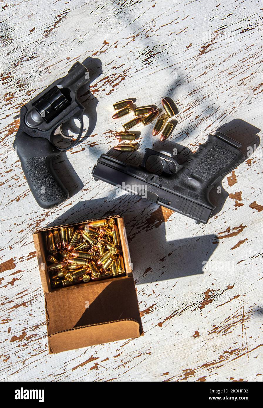 Una pistola semiautomatica 9mm Glck, una revolver Ruger da 9 mm, conchiglie e una scatola di cartucce in una scatola di cartone su un tavolo di legno. Foto Stock