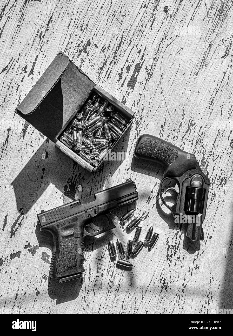 Una pistola semiautomatica 9mm Glck, una revolver Ruger da 9 mm, conchiglie e una scatola di cartucce in una scatola di cartone su un tavolo di legno. Foto Stock