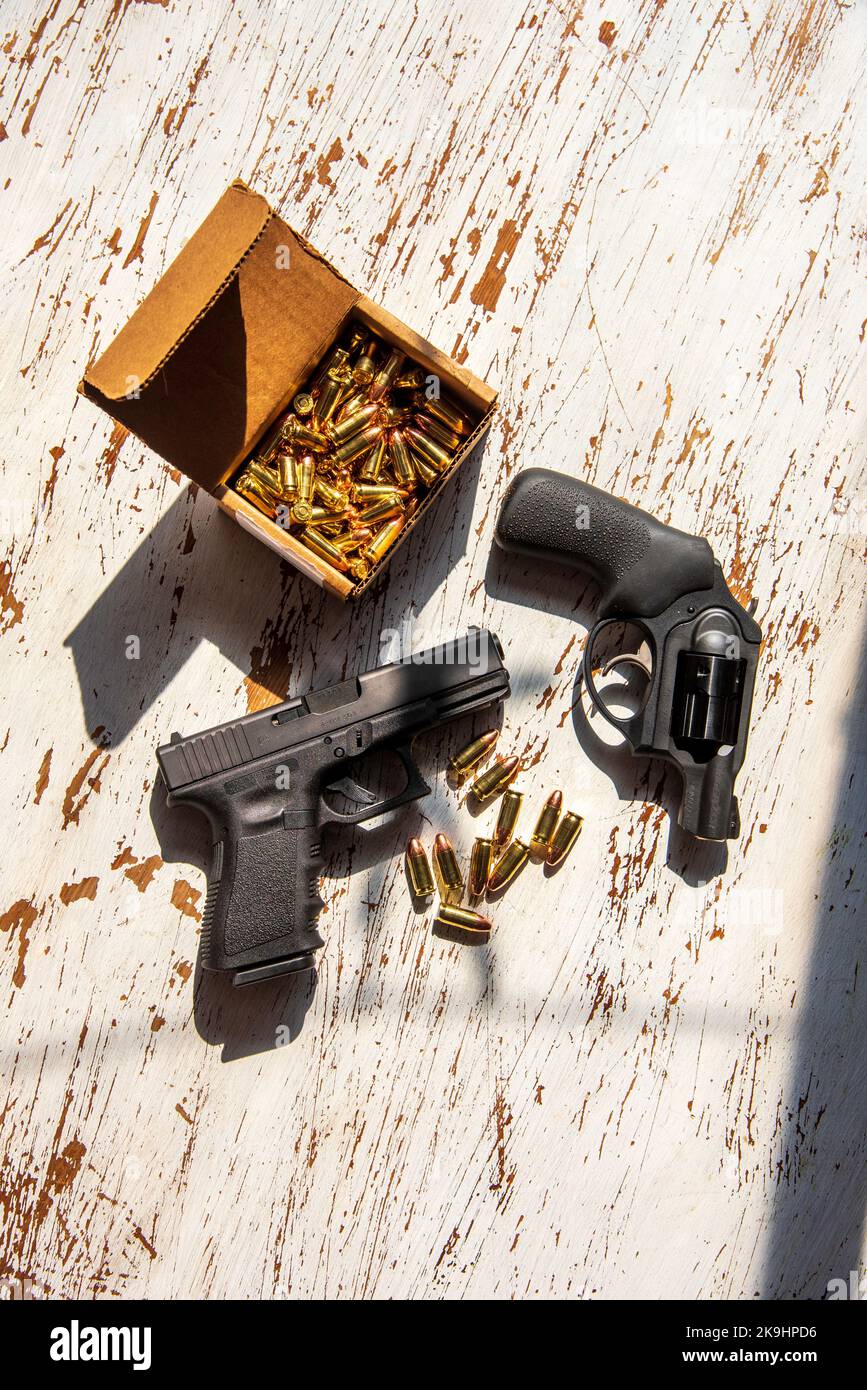 Una pistola semiautomatica 9mm Glck, una revolver Ruger da 9 mm, conchiglie e una scatola di cartucce in una scatola di cartone su un tavolo di legno. Foto Stock