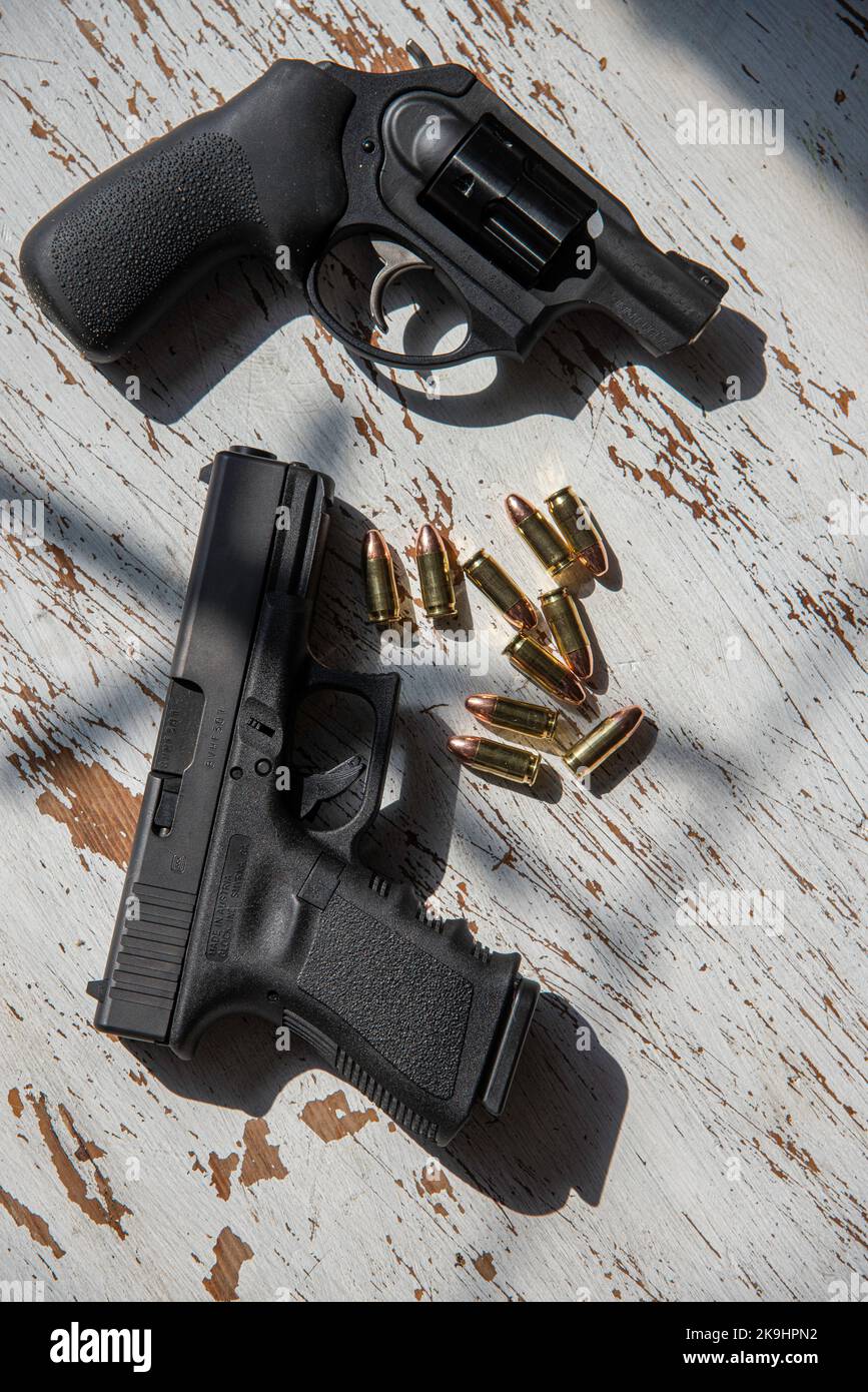 Un nero, Glock 19, 9mm, pistola e un Ruger, 9mm, snub naso, revolver su un tavolo di legno insieme con alcuni proiettili. Foto Stock