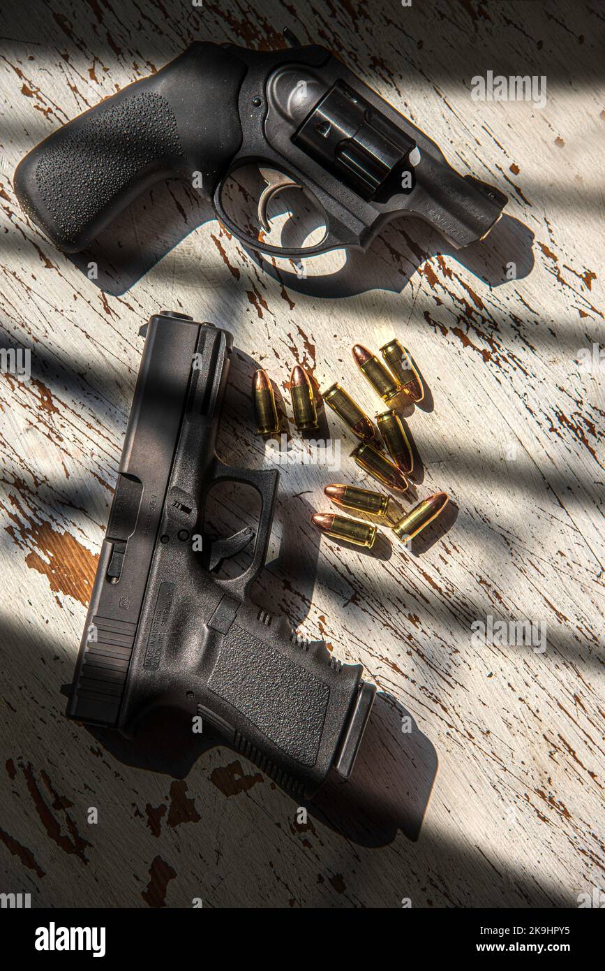 Un revolver Ruger 9mm, una pistola da 9mm Glock e una manciata di 9mm conchiglie, su un tavolo di legno. Foto Stock