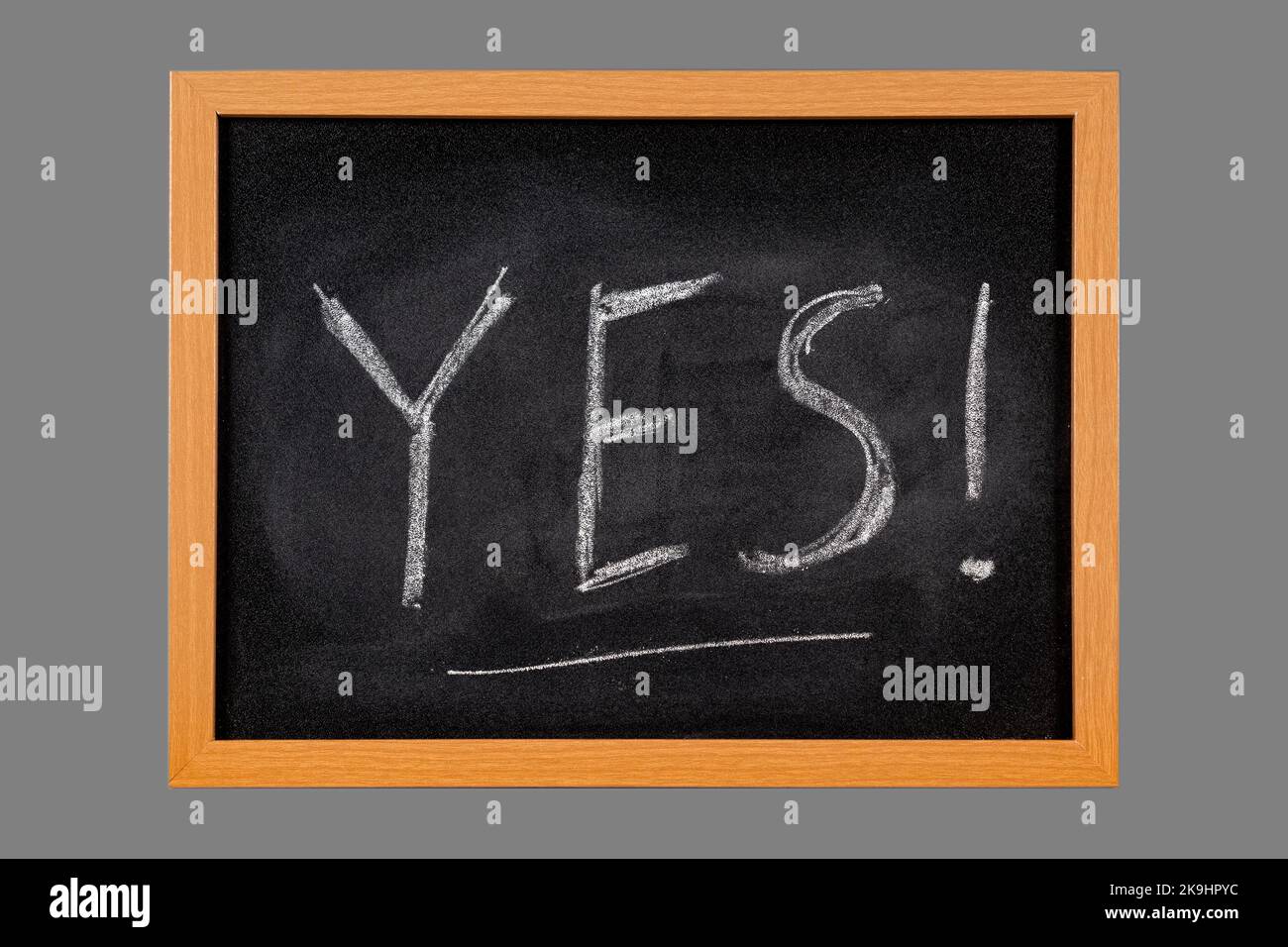 La parola Sì scritta a mano con gesso bianco su lavagna con cornice di legno, isolata su fondo grigio medio Foto Stock