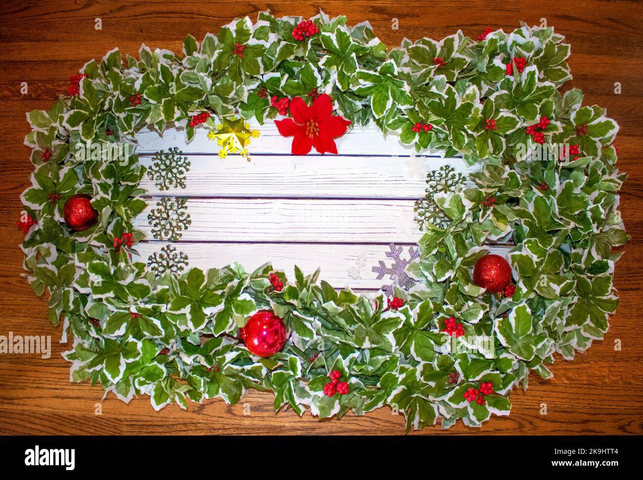 Tavole dipinte di bianco circondate da lussuose foglie di agrifoglio e palle di Natale e vari ornamenti fiocco di neve con spazio per la copia e ricco woo rifinito Foto Stock