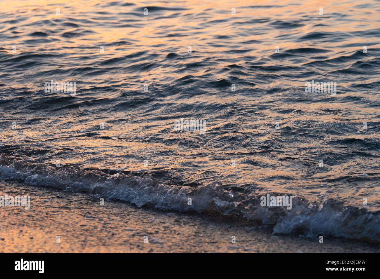 L'onda di mare spruzza da vicino. Ondulazione della superficie dell'acqua di mare con luce dorata del tramonto. Foto Stock