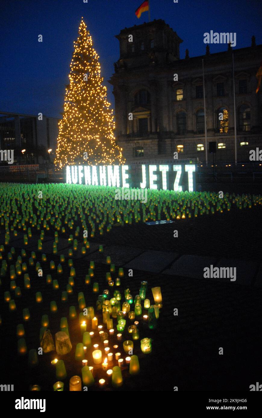 Un grande cartello illuminato, 'Aufnahme Jetzt' con molte tazze verdi con candele fuori dal Reichstag, Berlino, Germania. Foto Stock