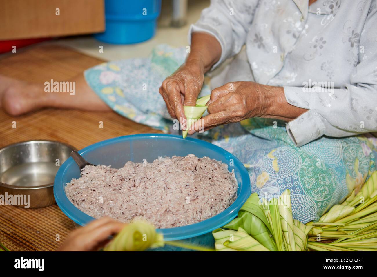 Mani di donna anziana che avvolgono il riso appiccicoso con foglie di palma o Ketupat Palas Foto Stock