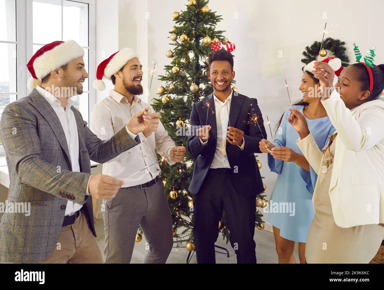 Amici multirazziali felici che celebrano il Natale parlando con gli scintillatori nelle mani vicino all'albero di Natale. Foto Stock